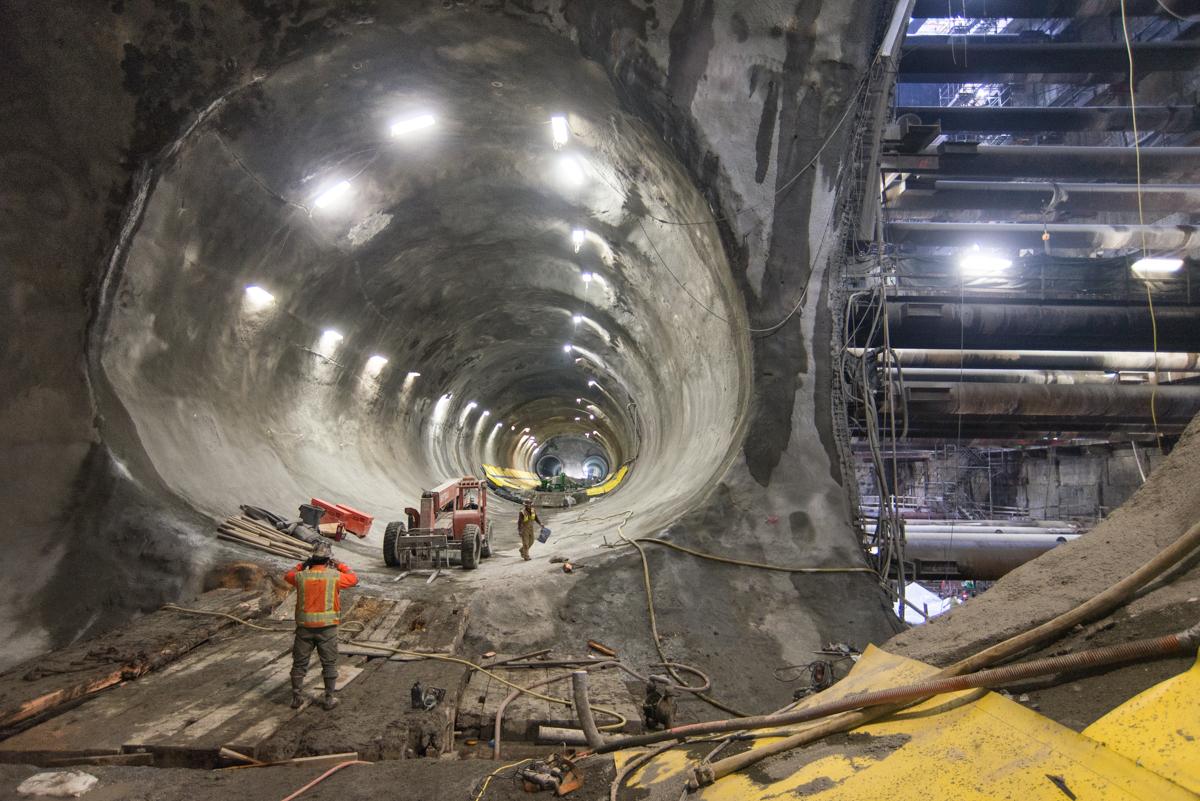 Workers in hard hats inside a large circular tunnel under construction with LED lighting and equipment visible.