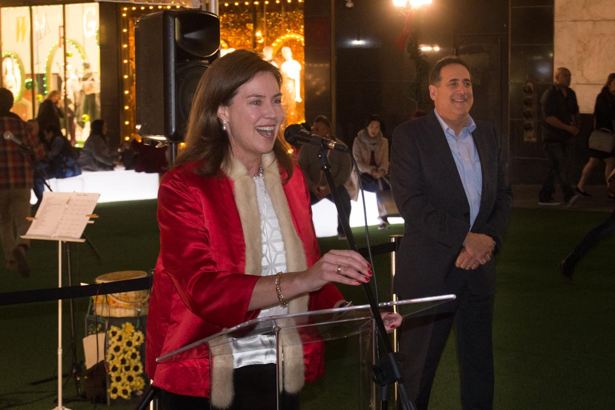 Woman in red blazer speaking at podium during transit project opening ceremony