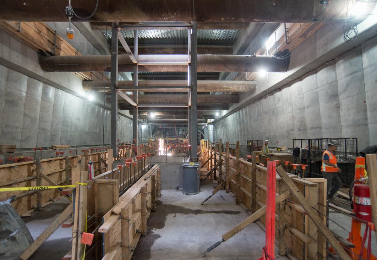 Interior construction site with wooden forms and concrete foundation work for future transit station platform.