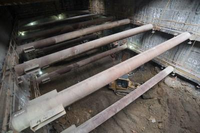 Underground construction site showing temporary steel support beams spanning across an excavated station headhouse structure.