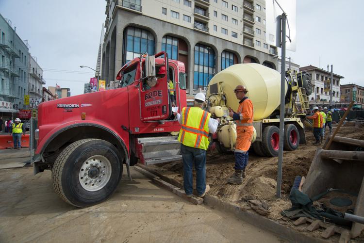 Red cement mixer truck with workers in safety vests at Chinatown Station construction site on Stockton Street.