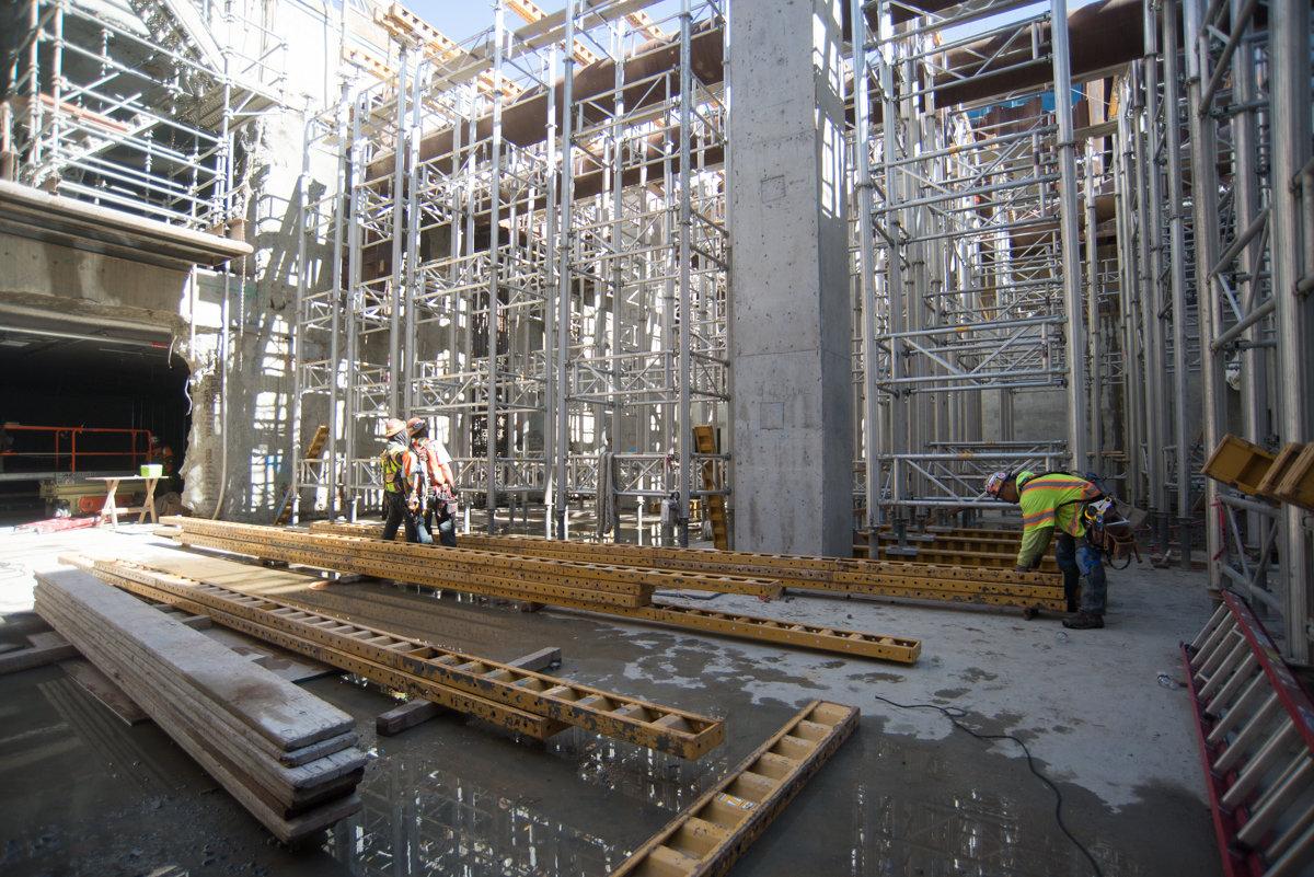Construction site with metal scaffolding, concrete columns, and workers in safety gear on wet ground.