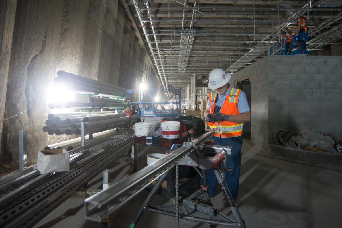 Worker in safety gear fabricating conduit bracket on station concourse level during construction.