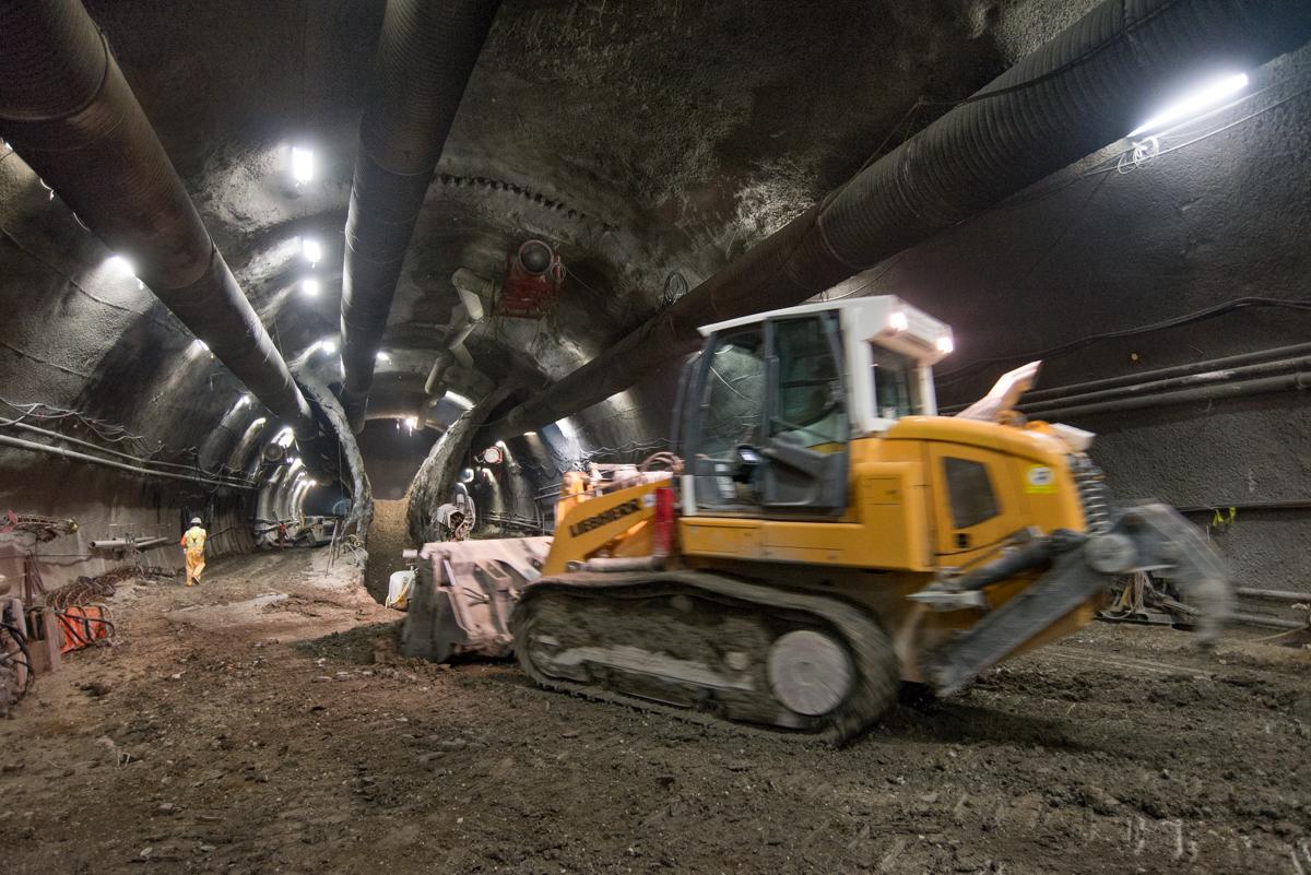 Yellow bulldozer excavating material inside underground tunnel with LED lighting and workers present.