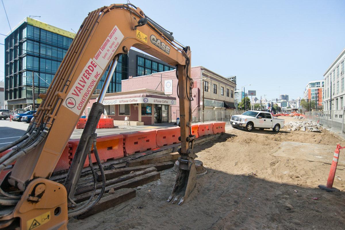Construction excavator and orange barriers at tunnel portal ramp entrance during utility work preparation.
