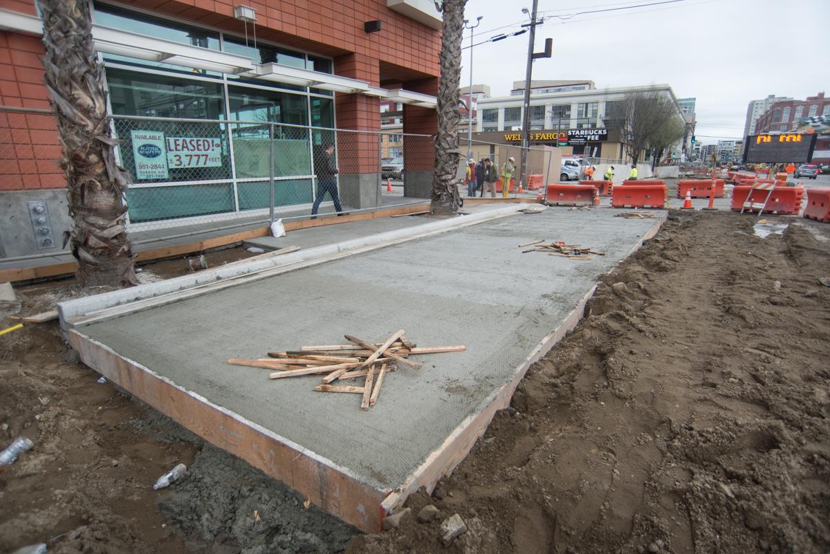Construction site on 4th Street with concrete foundation, wooden debris, and red barriers along urban street.