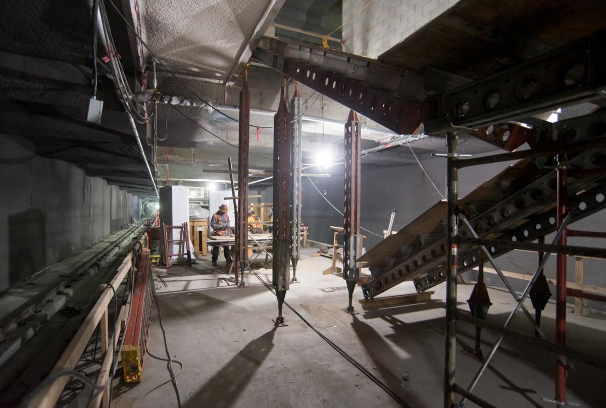 Worker prepares rigging to lift PVC conduit with crane at transit station mezzanine level.