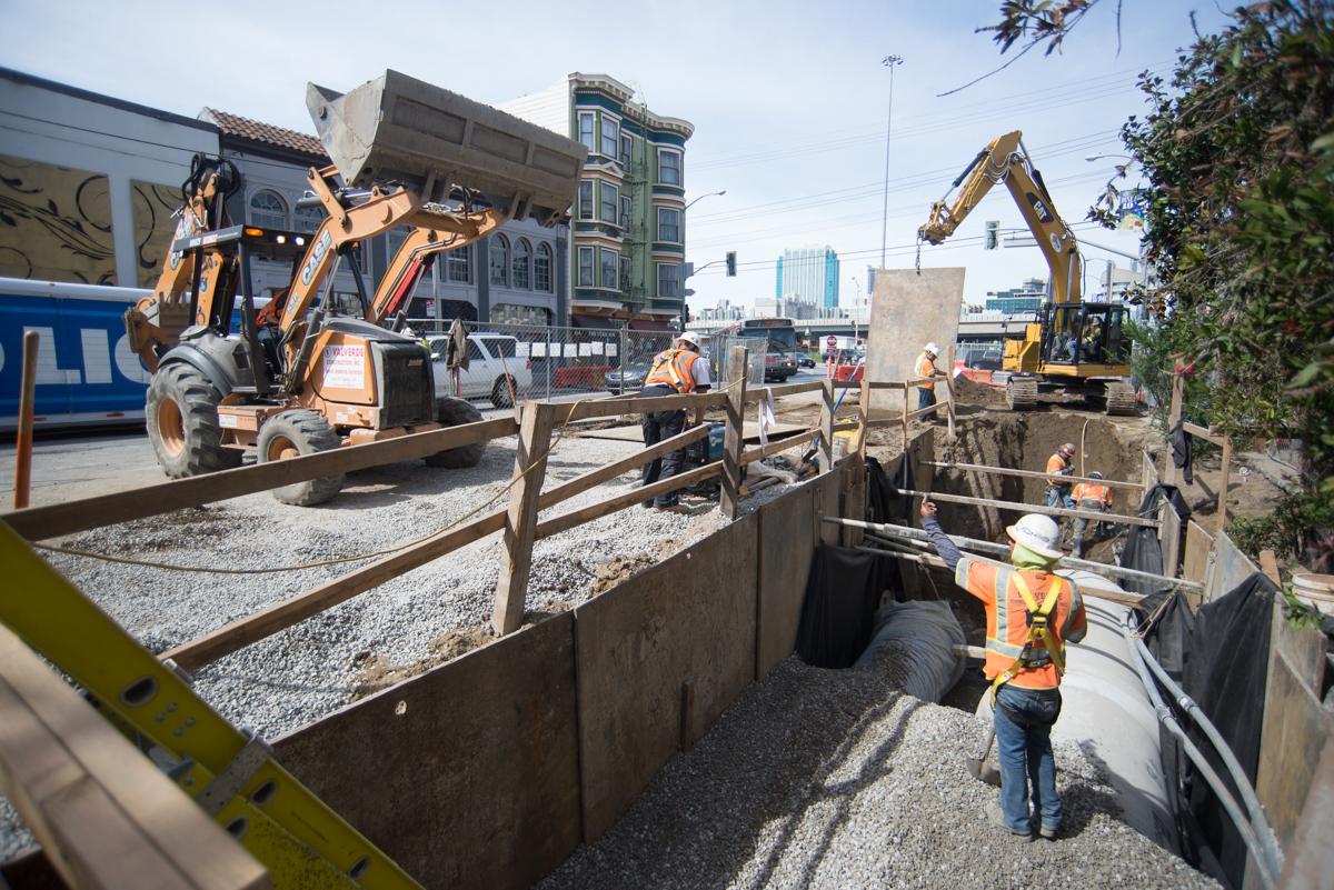 Construction workers and equipment excavating a trench for underground utility installation on an urban street.