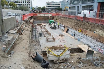 Construction site at Yerba Buena/Moscone Station showing excavation, equipment, and workers installing roof deck structures.