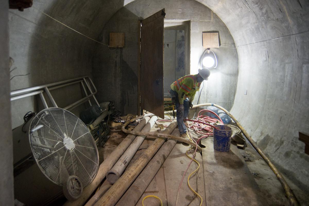 Worker in safety gear inspecting equipment inside subway tunnel cross passage during construction.
