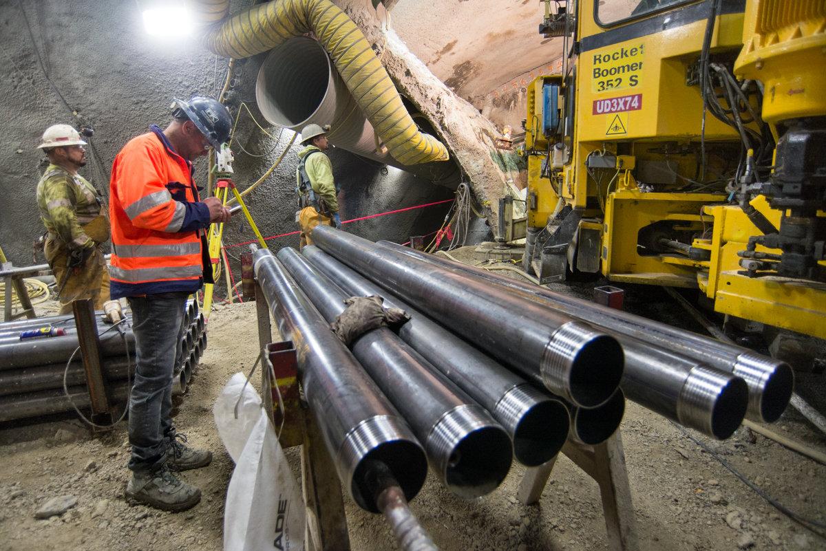 Workers in safety gear prepare large steel pipe sections for underground installation at a construction site.