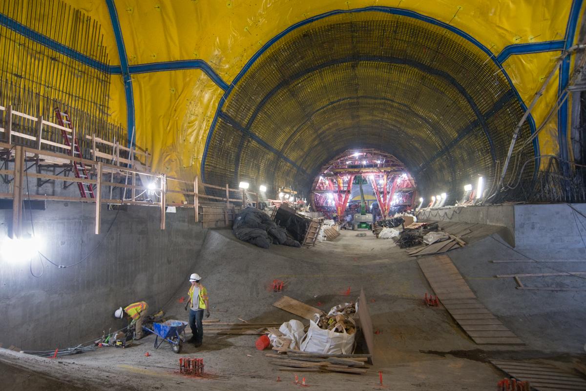 Workers construct platform cavern inside Chinatown Station tunnel with yellow support structure and concrete walls.