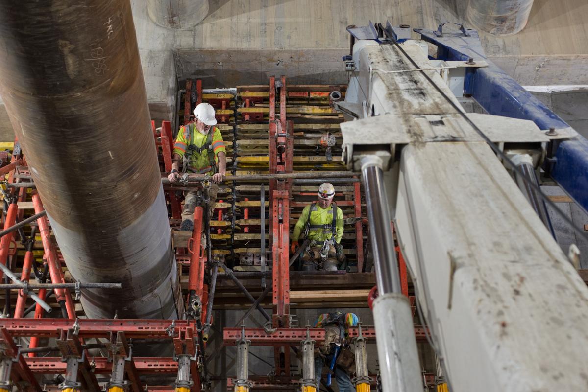 Workers in safety gear on red scaffolding inside underground transit station construction site.