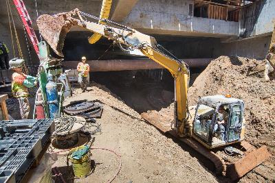 Excavation work at Chinatown Station with yellow mini excavator and construction workers on site.