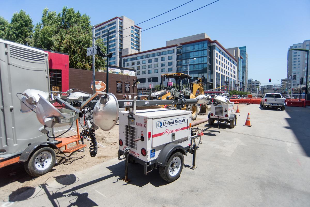 Construction equipment and utility vehicles parked at a 4th Street worksite with residential buildings in background.