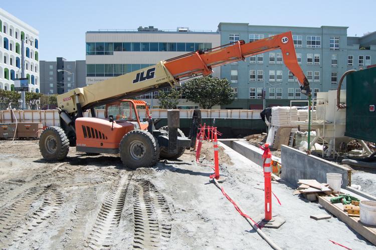 Red and tan telescopic handler on construction site with guide wall forms and safety barriers