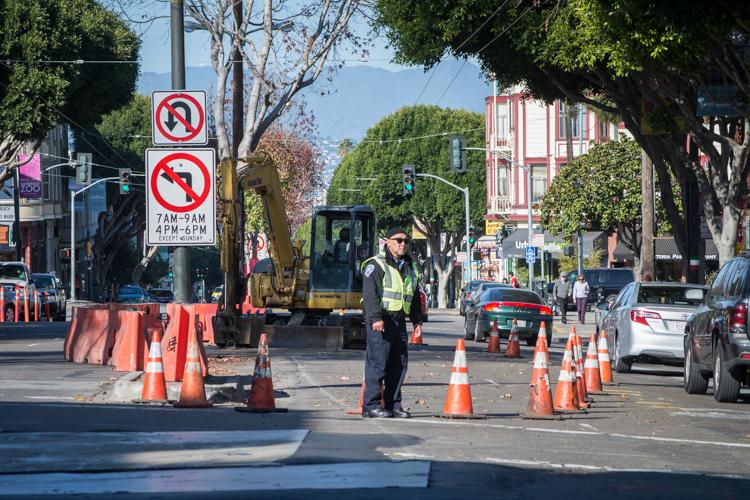 Construction site on urban street with excavator, traffic cones, and worker in safety vest managing street closure.