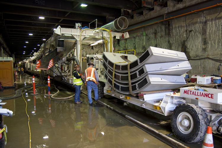 Workers load concrete tunnel segments onto a truck at an underground construction site with a tunnel boring machine.