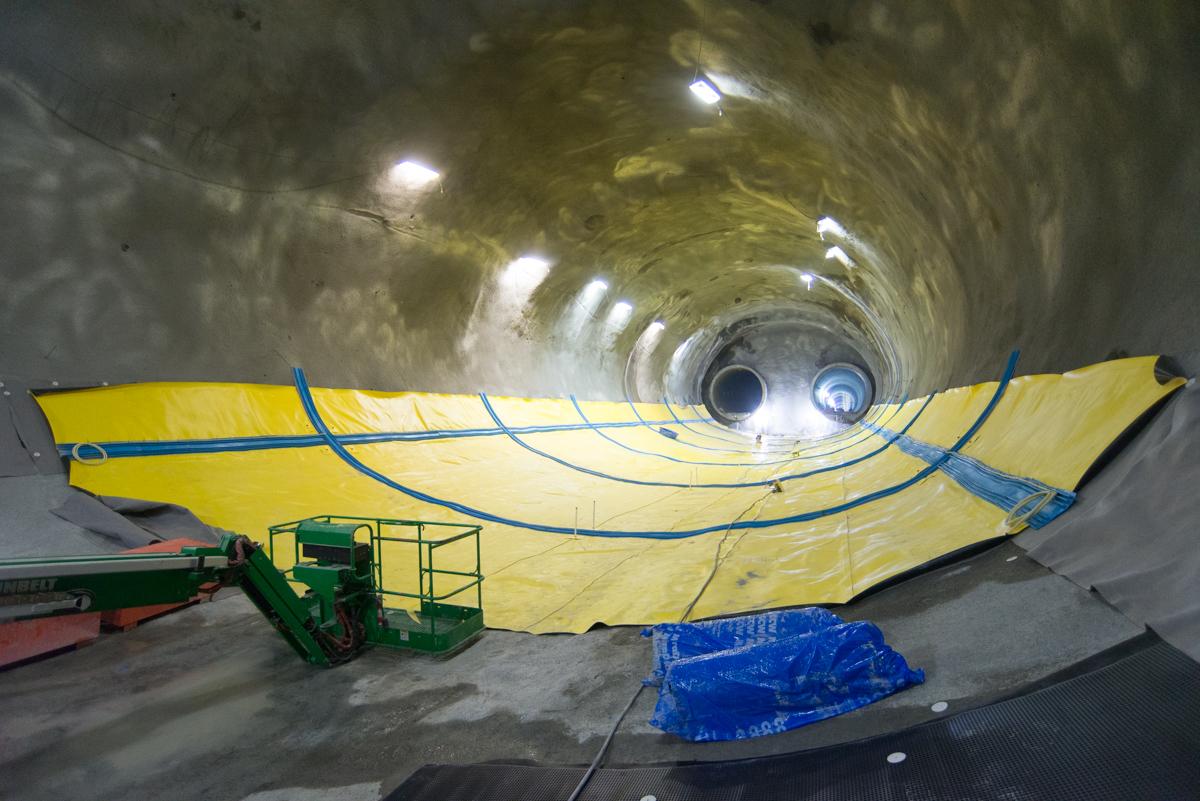 Yellow waterproofing membrane sheets installed inside underground transit tunnel with construction equipment and lighting.