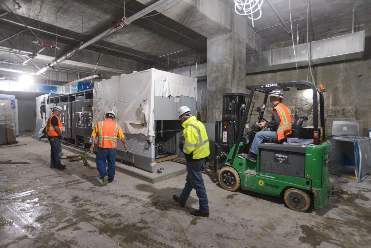 Workers in safety vests operate a forklift while installing equipment in an underground transit station under construction.
