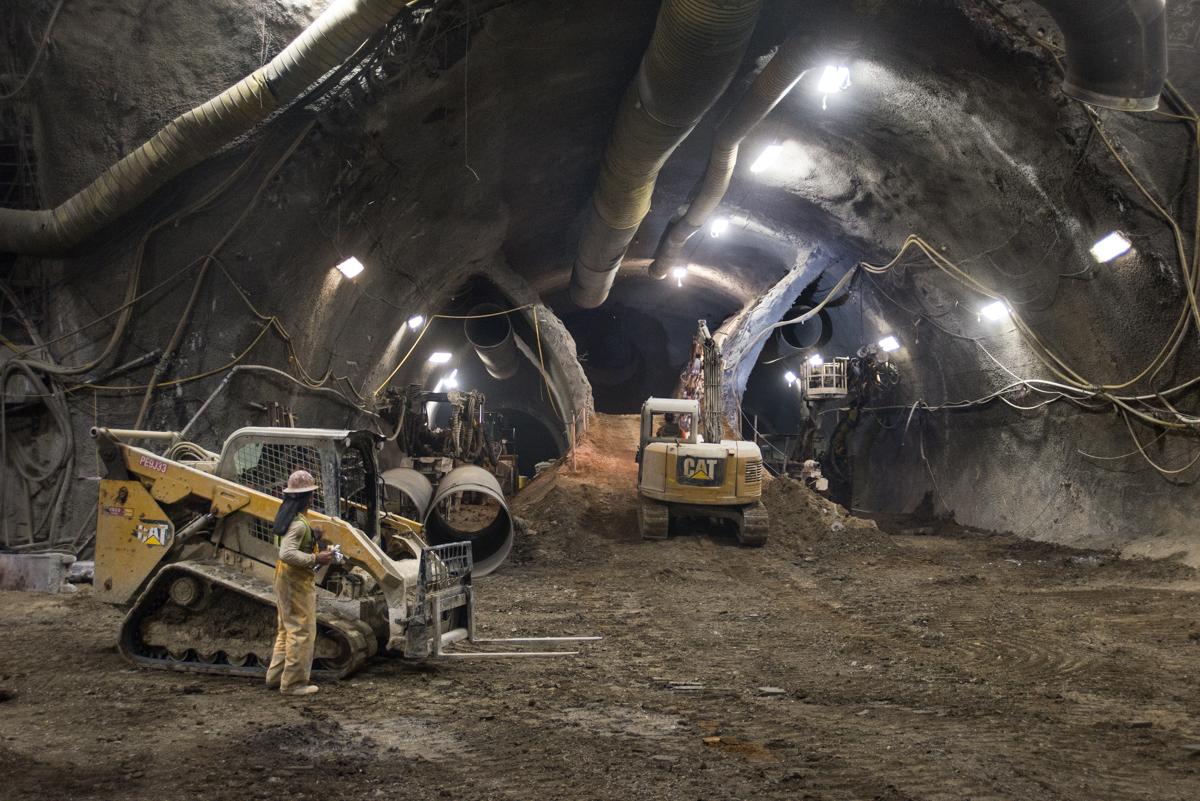 Underground tunnel construction site with yellow CAT excavators and bulldozers working in lit cavern.