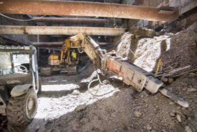 Construction site with excavator, jackhammer equipment, and debris during underground transit station headhouse excavation work.