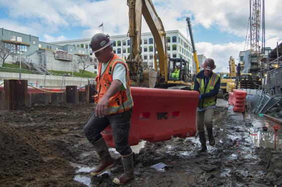 Construction workers in safety vests move a red barrier at the Yerba Buena/Moscone Station excavation site.