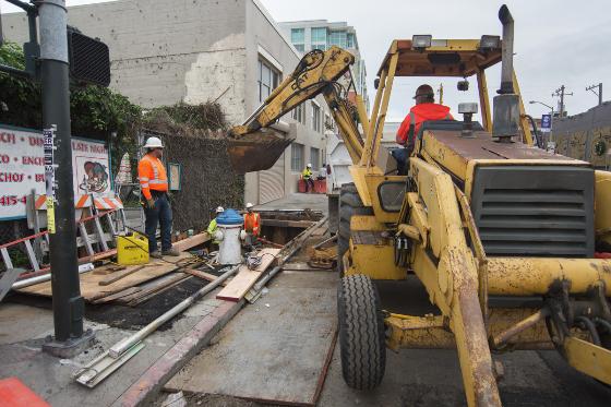 Construction crew operates excavator to install utility vault on city street.