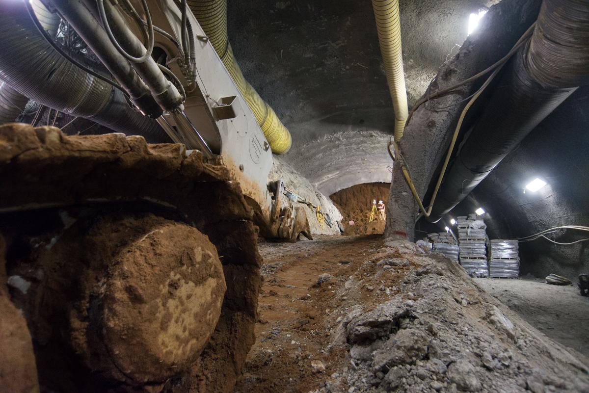 Underground tunnel construction site with surveyor, equipment, and exposed rock walls lit by work lights.