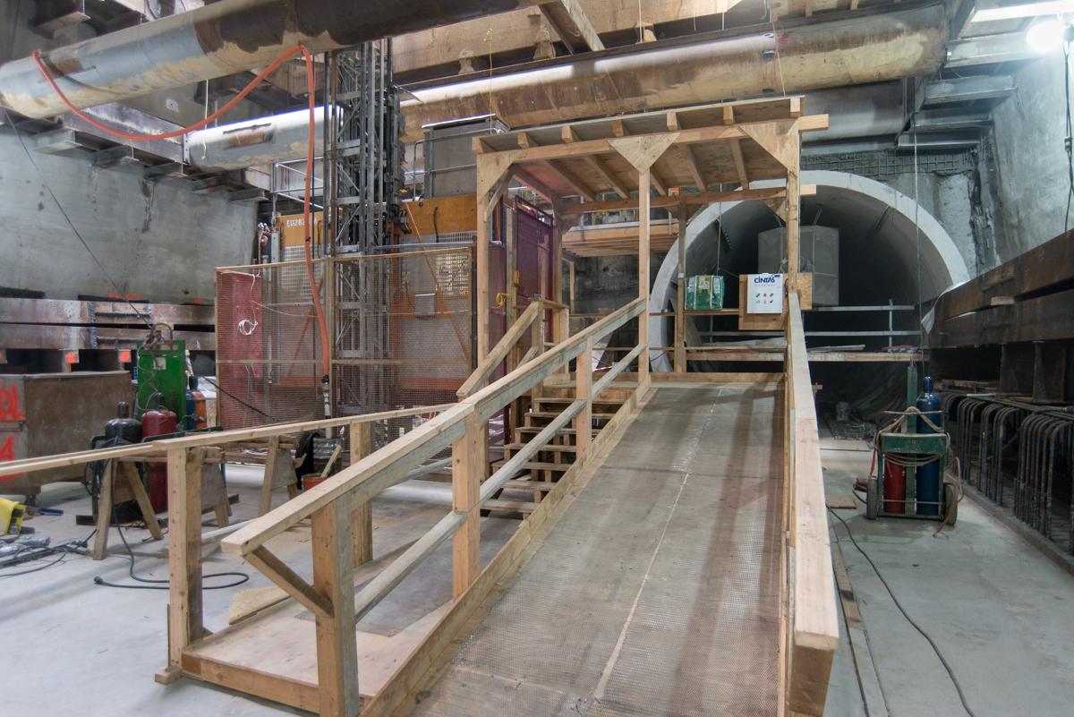 Construction site showing wooden platform and crew elevator installed in underground transit station excavation.