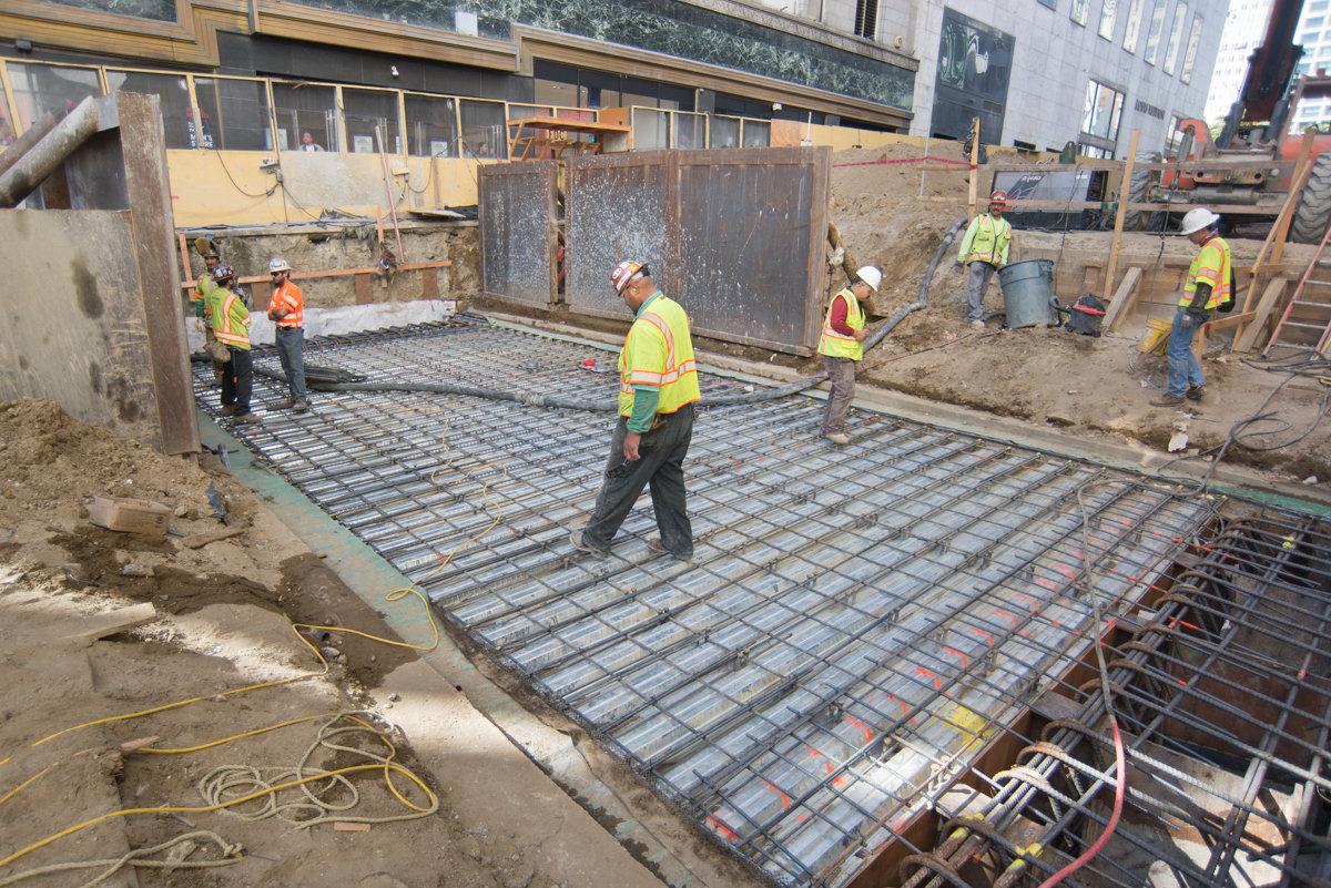 Construction workers laying rebar grid for concrete foundation at transit station site.