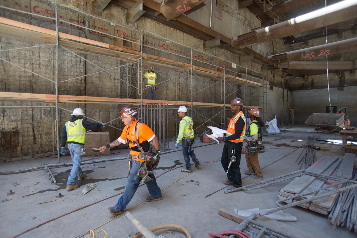 Construction workers in safety gear review plans inside a transit station under renovation.