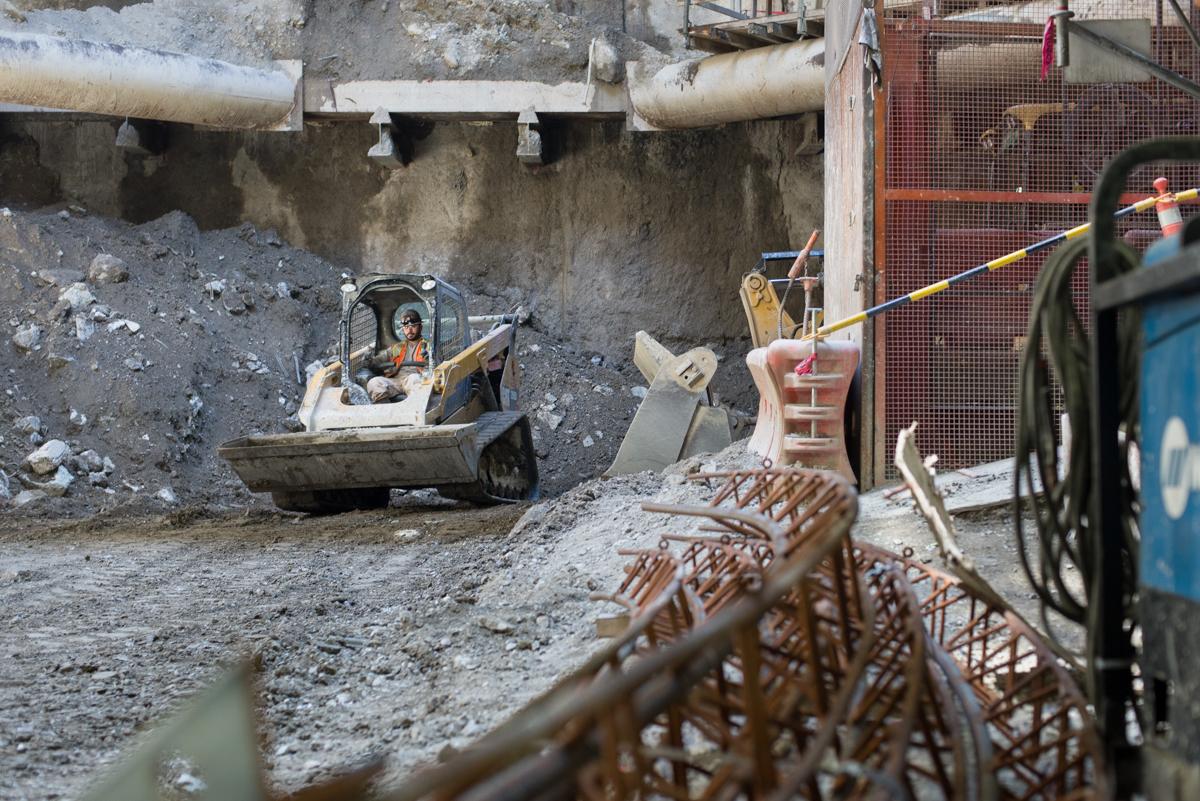 Construction equipment and materials at underground transit station excavation site with steel reinforcement mesh visible.