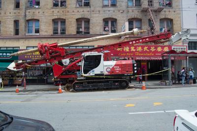 Red drill rig parked on Stockton Street with construction equipment and barriers visible.