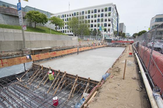 Construction site with concrete foundation, reinforced steel mesh, and safety barriers along 4th Street.