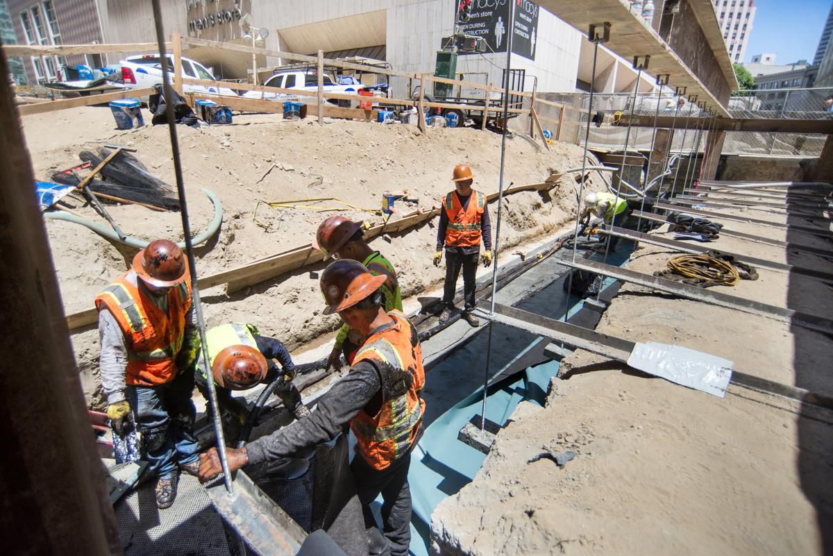 Construction workers in safety gear installing waterproofing on station roof deck at 4th and Clementina Streets.
