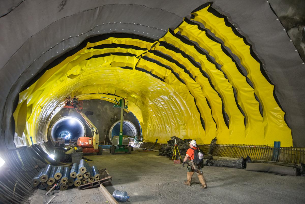 Chinatown tunnel under construction with yellow waterproofing material and construction equipment visible inside.