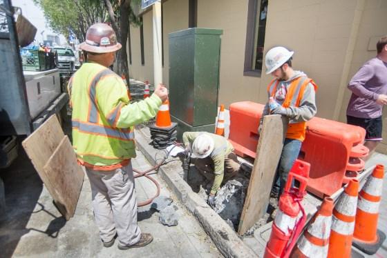 Construction workers install overhead catenary system pole foundations on 4th Street.