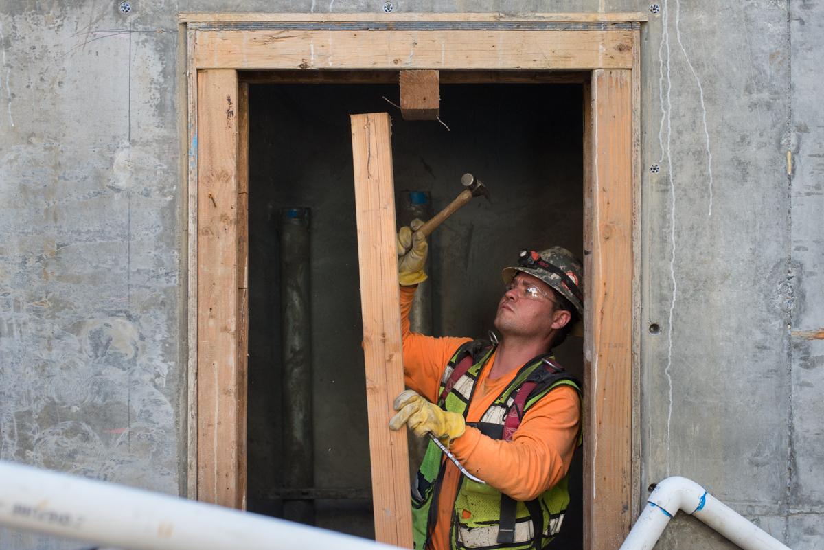 Worker in safety gear removing concrete formwork from doorway opening at transit station headhouse.