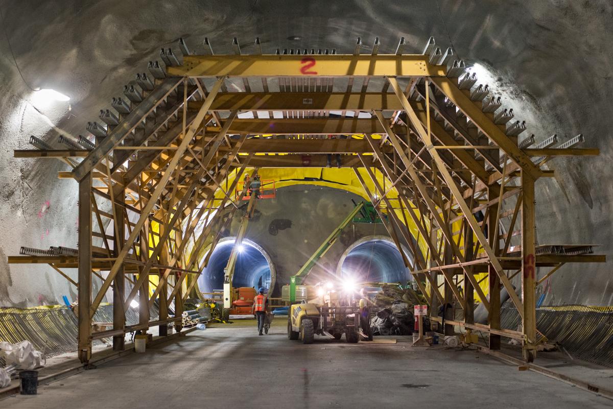 Construction tunnel with yellow scaffolding, large circular tunnel boring machine segments, and workers with equipment.