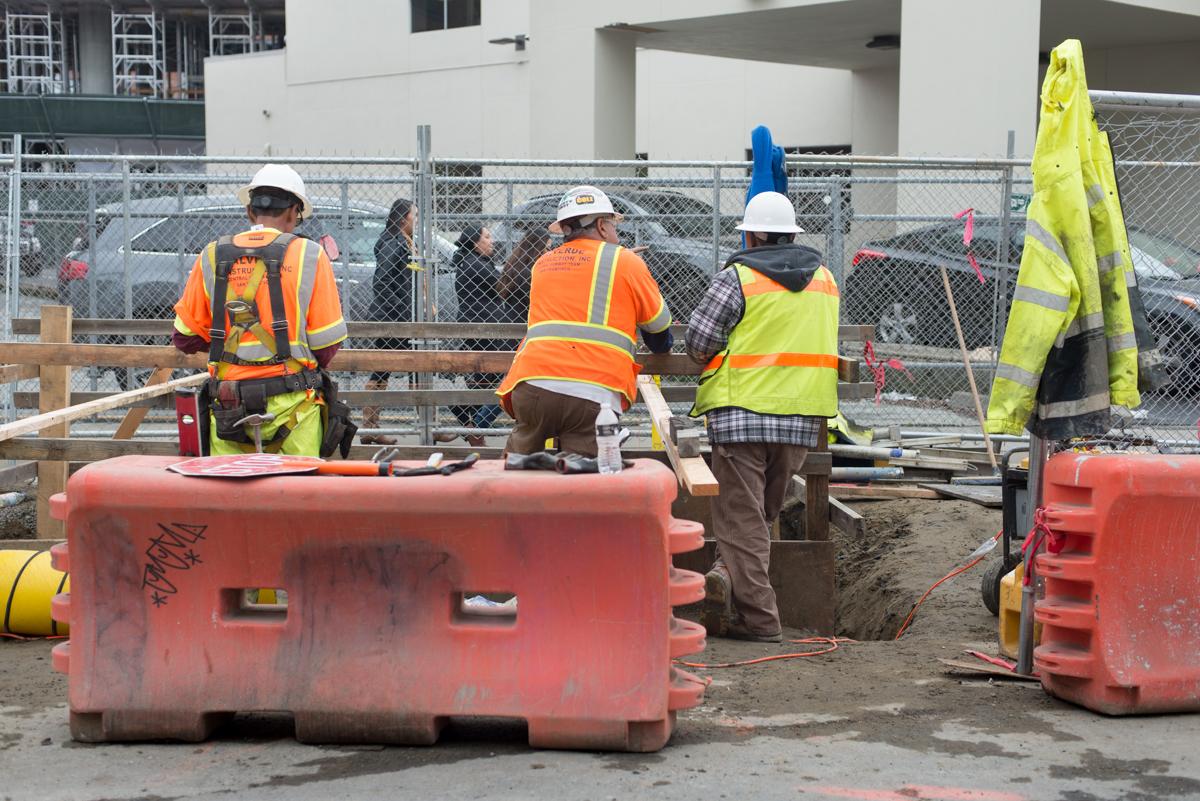 Construction workers in safety vests and hard hats work on 4th Street roadway restoration project.
