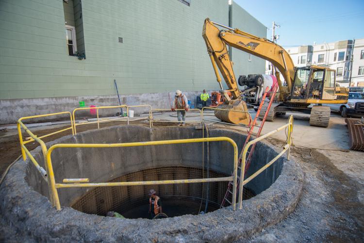 Construction shaft being excavated at 1455 Stockton Street with yellow safety barriers and excavator equipment on site.