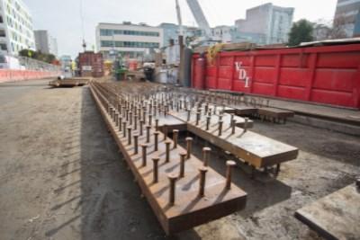 Steel reinforcement plates staged on construction site next to red equipment truck and excavation area.
