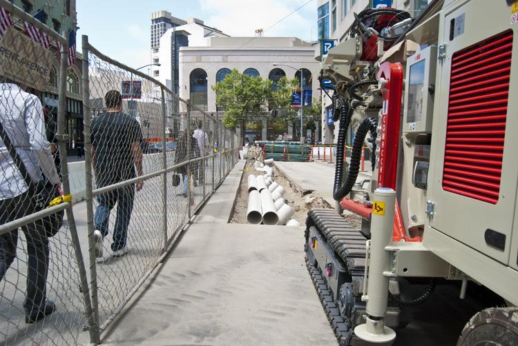 Construction site on 4th Street with fencing, pipes, and equipment visible along sidewalk.
