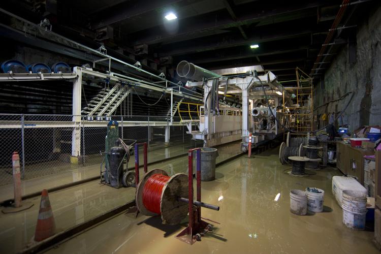 Flooded industrial workshop with tunnel boring machine trailing gear assembly, red cable spool, and construction equipment.