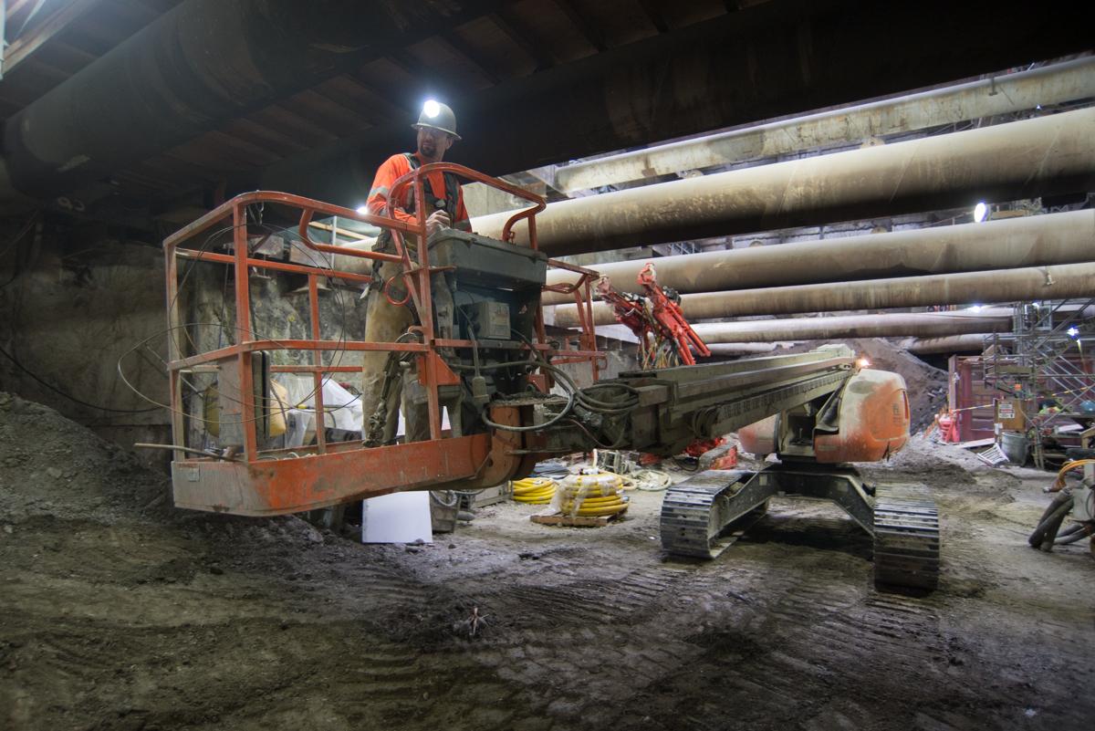 Worker in elevated basket operating machinery inside underground transit station during construction.