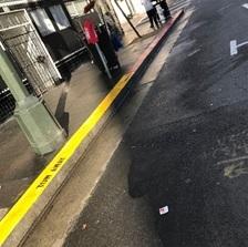 Yellow curb marking on urban street with sidewalk and pedestrians visible.