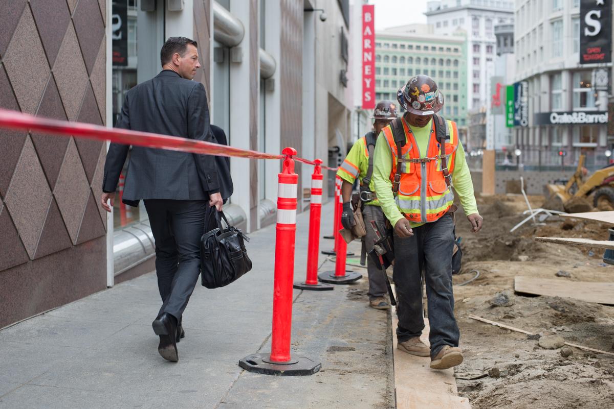 Man in business suit walking past construction worker on closed sidewalk at 4th Street.