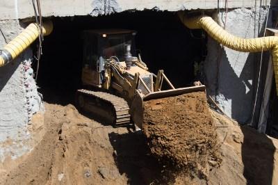Bulldozer exiting tunnel portal with excavated soil during underground station construction.