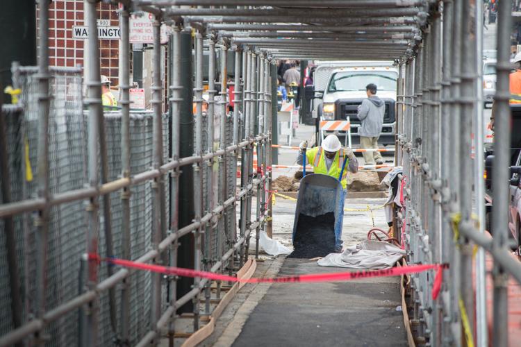 Construction worker in safety vest and hard hat inside fenced walkway at Chinatown Station construction site.